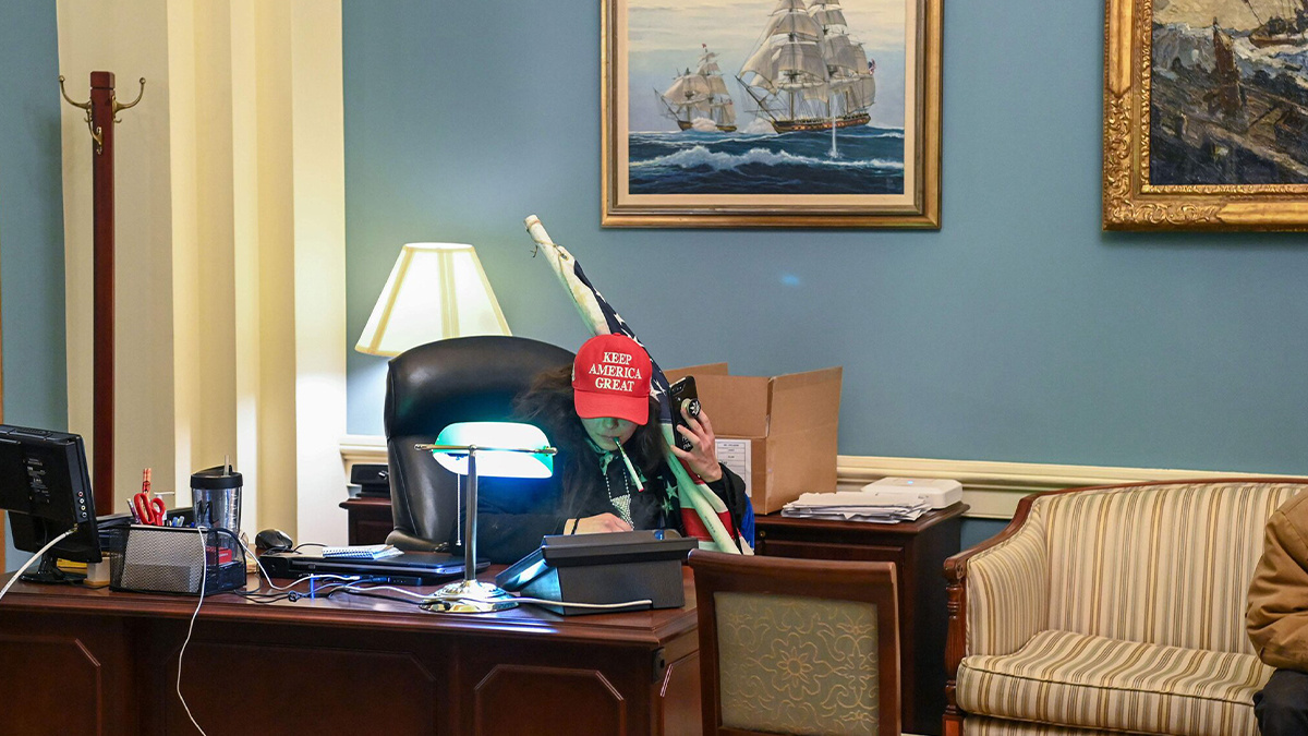 A woman wearing a MAGA hat sits in a government office after Trump supporters raided the Capitol Building 